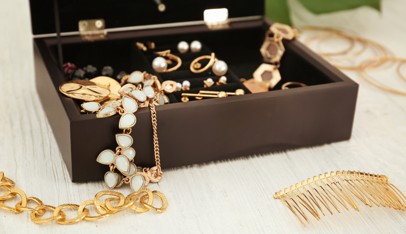 An open black jewelry box filled with a variety of gold and pearl accessories, including bracelets and earrings.