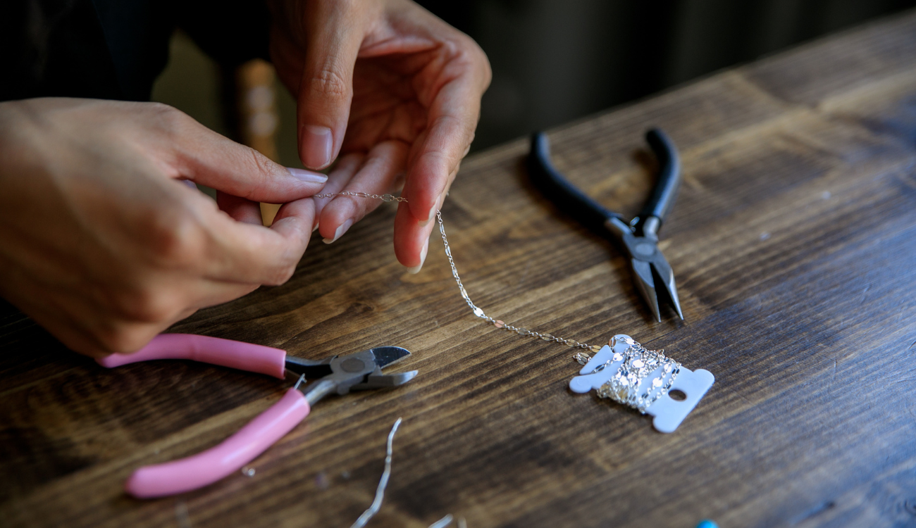 Hands working with jewelry-making pliers and a delicate chain, showing the process of creating a custom piece of jewelry.