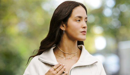 CC Crawford in a serene outdoor setting, wearing layered necklaces, hoop earrings, and gold rings, highlighting her effortless style.