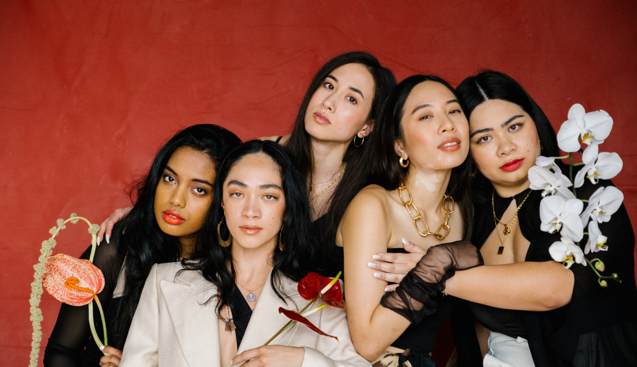 Group of diverse women wearing various floral-inspired jewelry pieces against a bold red background.