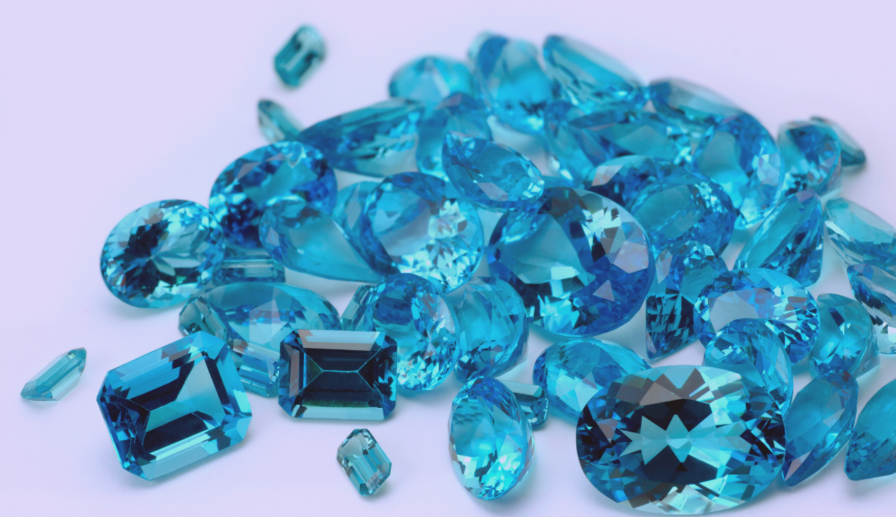 A collection of loose, faceted aquamarine gemstones in various cuts and sizes, displaying their radiant blue hues.