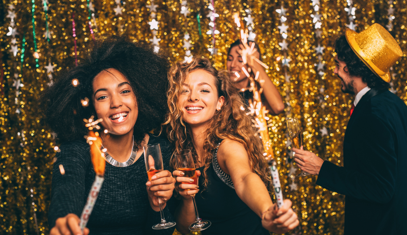 Group of friends celebrating New Year’s Eve with sparklers, champagne, and festive outfits.