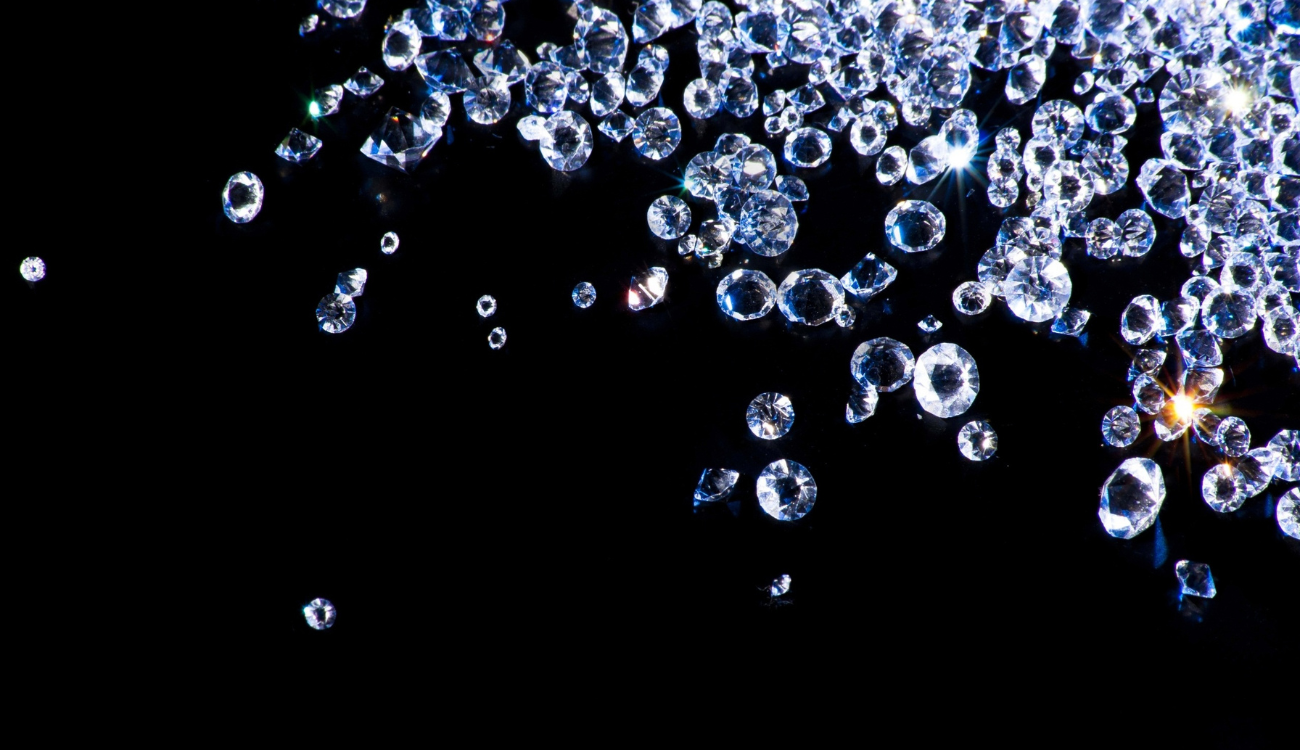 A scattered display of sparkling clear gemstones on a black background